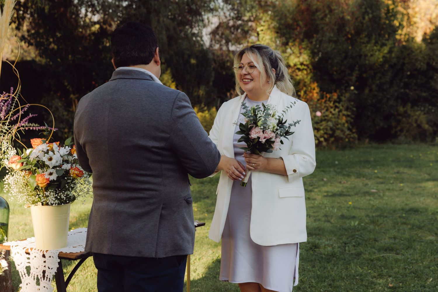 Bride holding bouquet smiles at groom during outdoor garden wedding ceremony.