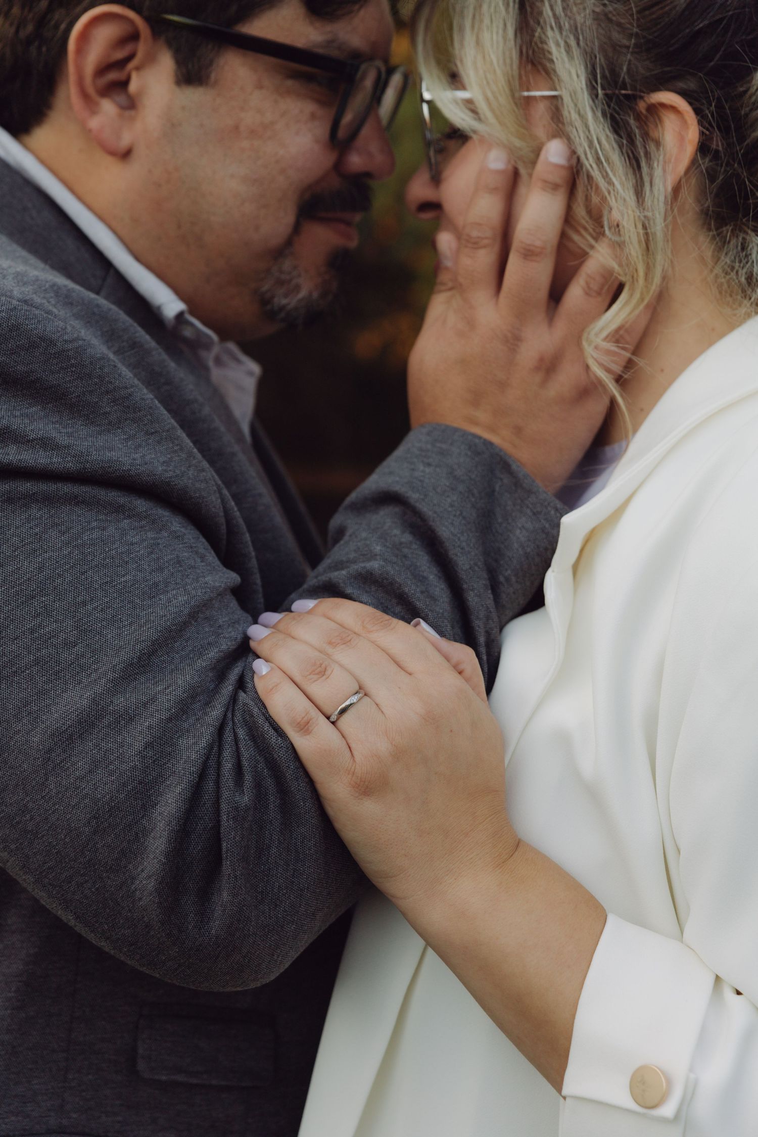 Intimate moment of couple touching foreheads, showcasing wedding rings during romantic outdoor garden ceremony.