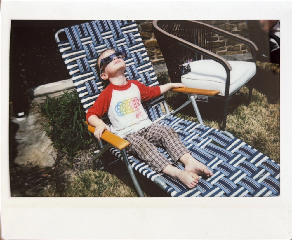 A person relaxes in a blue and white patterned lounge chair on a sunny patio.