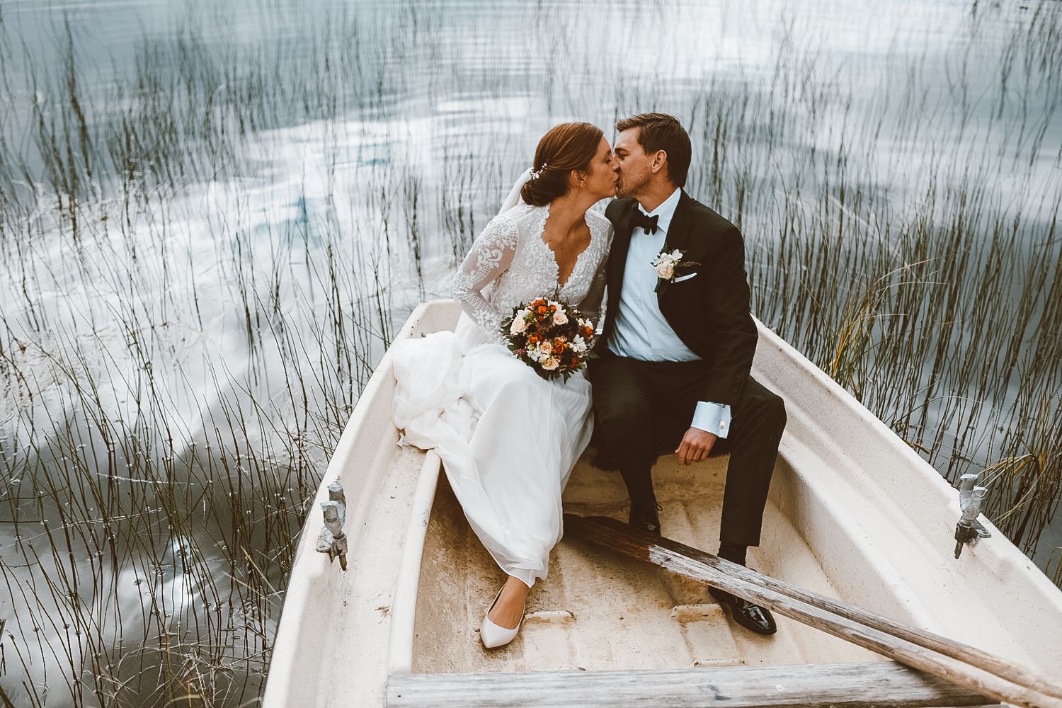Romantic moment between newlyweds sitting in a white rowboat on misty water.