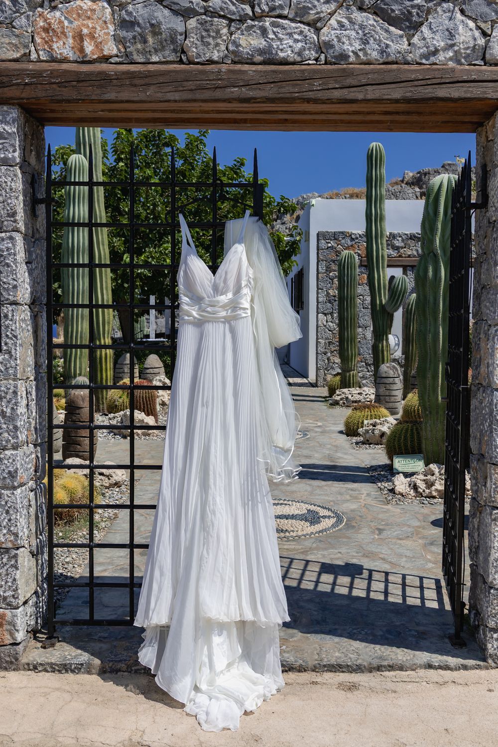 White wedding dresses displayed in a stone courtyard with tall cactus plants and archways creating a desert-chic setting.
