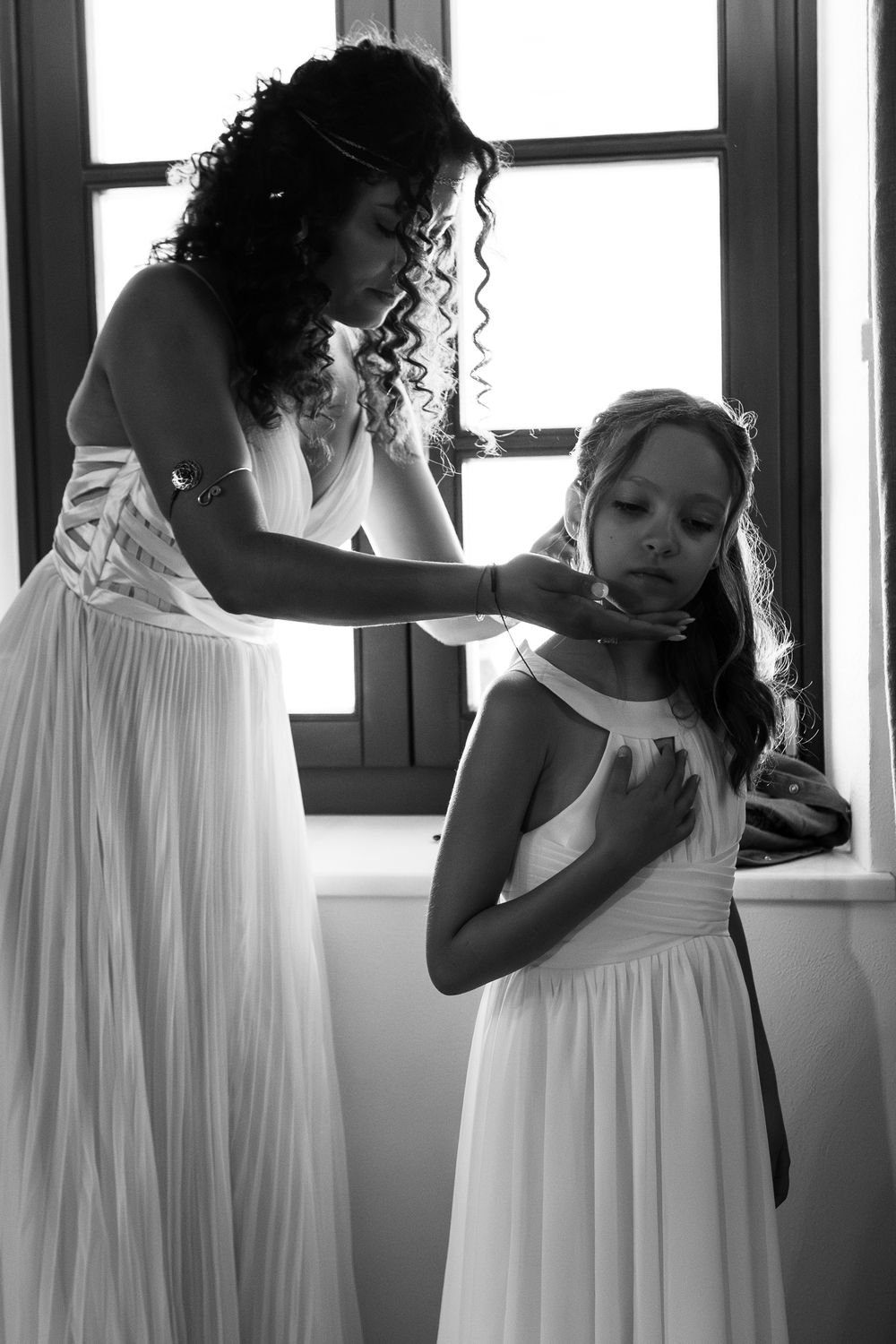 A series of black and white photos showing people in white dresses getting ready indoors by a window.