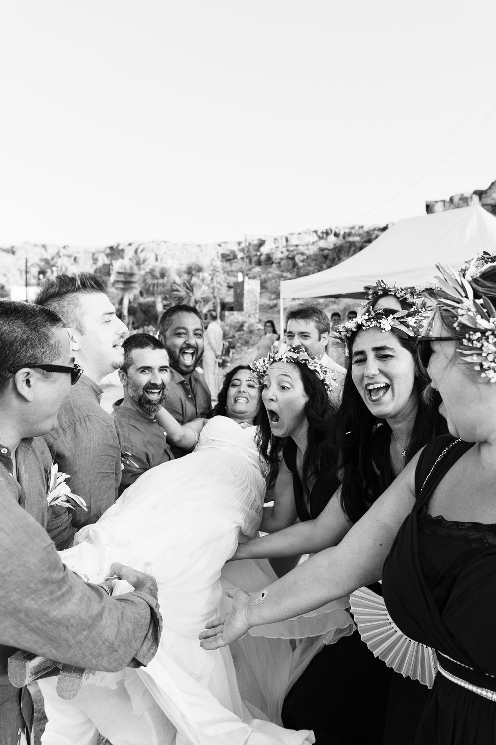 A joyful group of wedding guests laugh together during a celebratory moment at an outdoor reception.