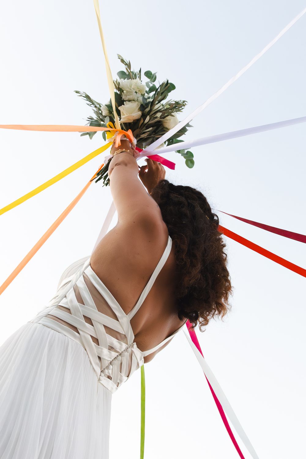 A person in a white dress with natural curly hair adorned with foliage stands against a colorful striped background.