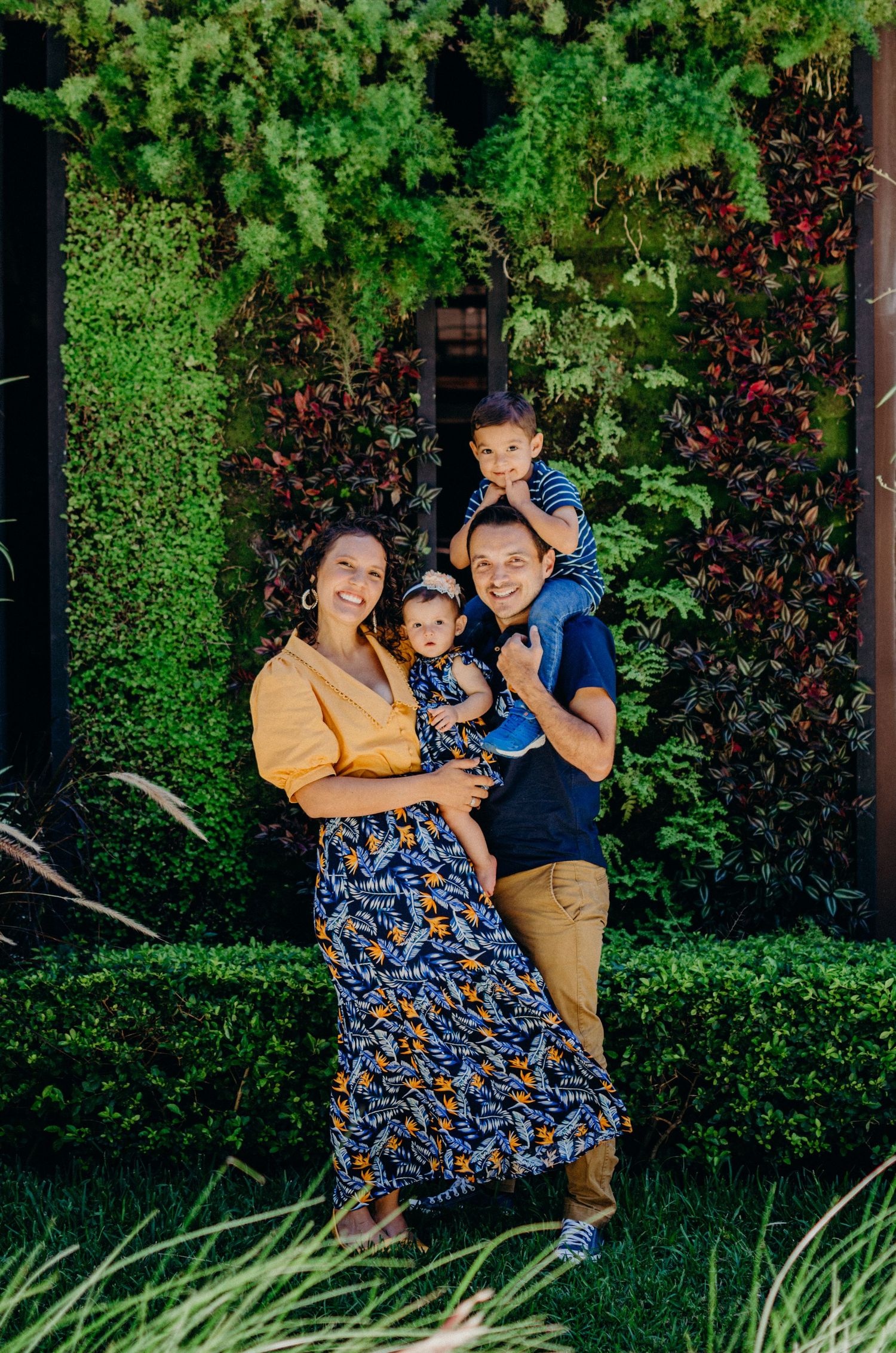 A family poses together in front of a lush green wall with vibrant foliage.