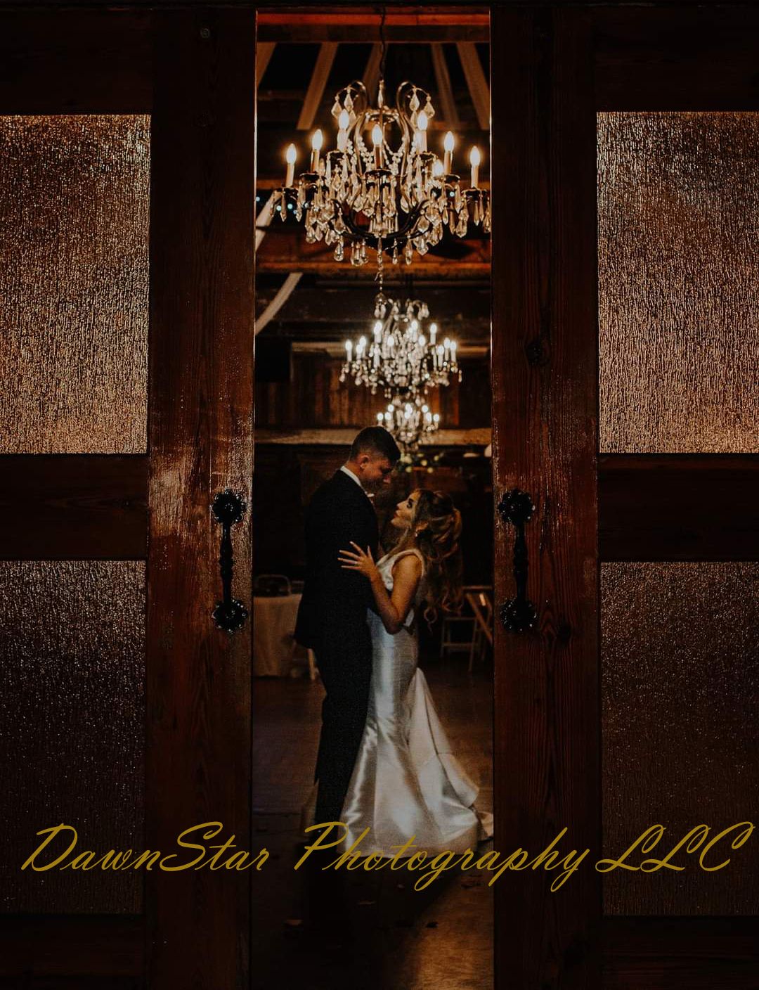 Bride in strapless wedding dress dances beneath ornate chandeliers in dimly lit rustic reception venue.