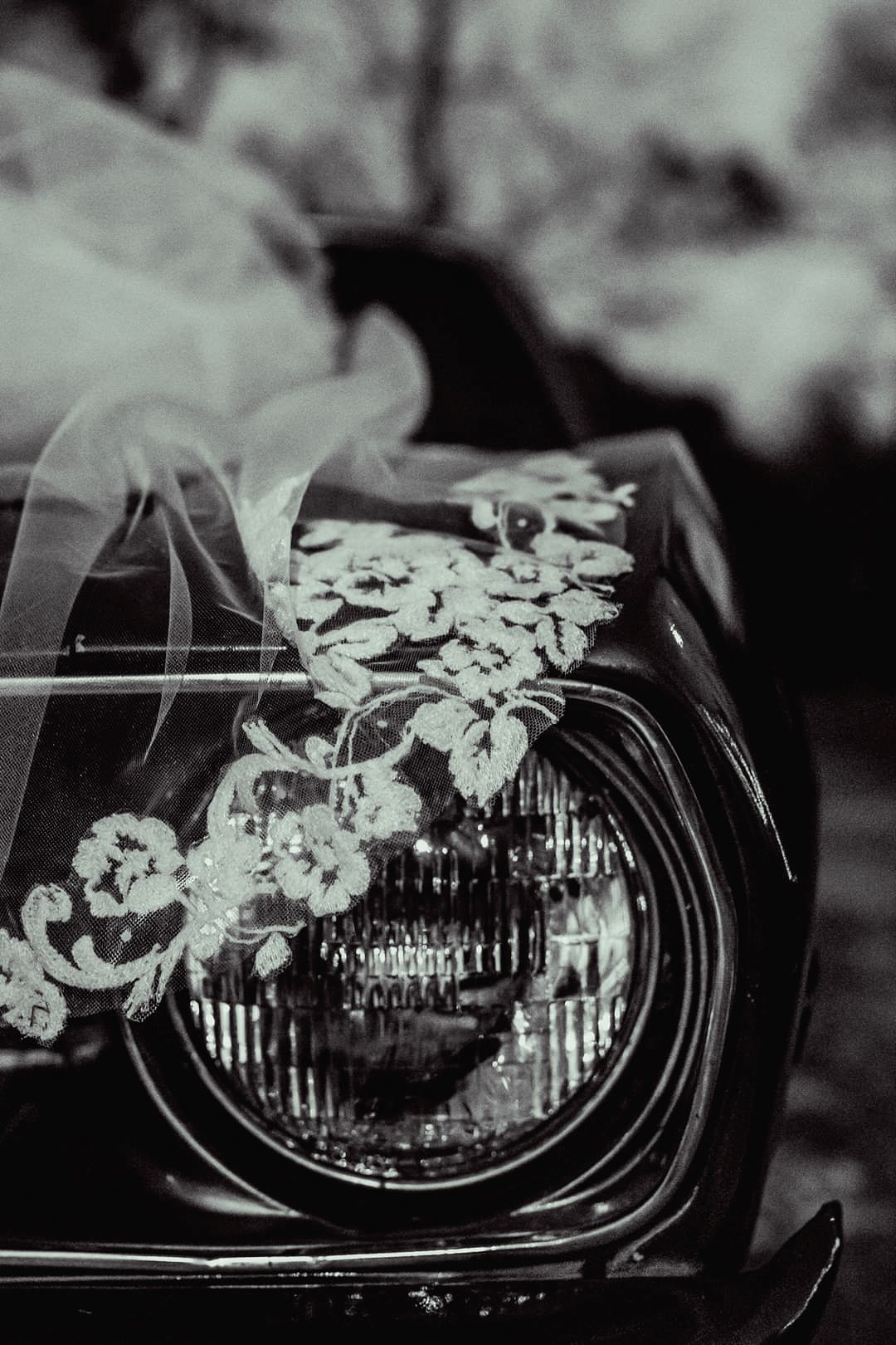 Black and white artistic photograph series showing a car headlight with flowers reflected in its glass surface.