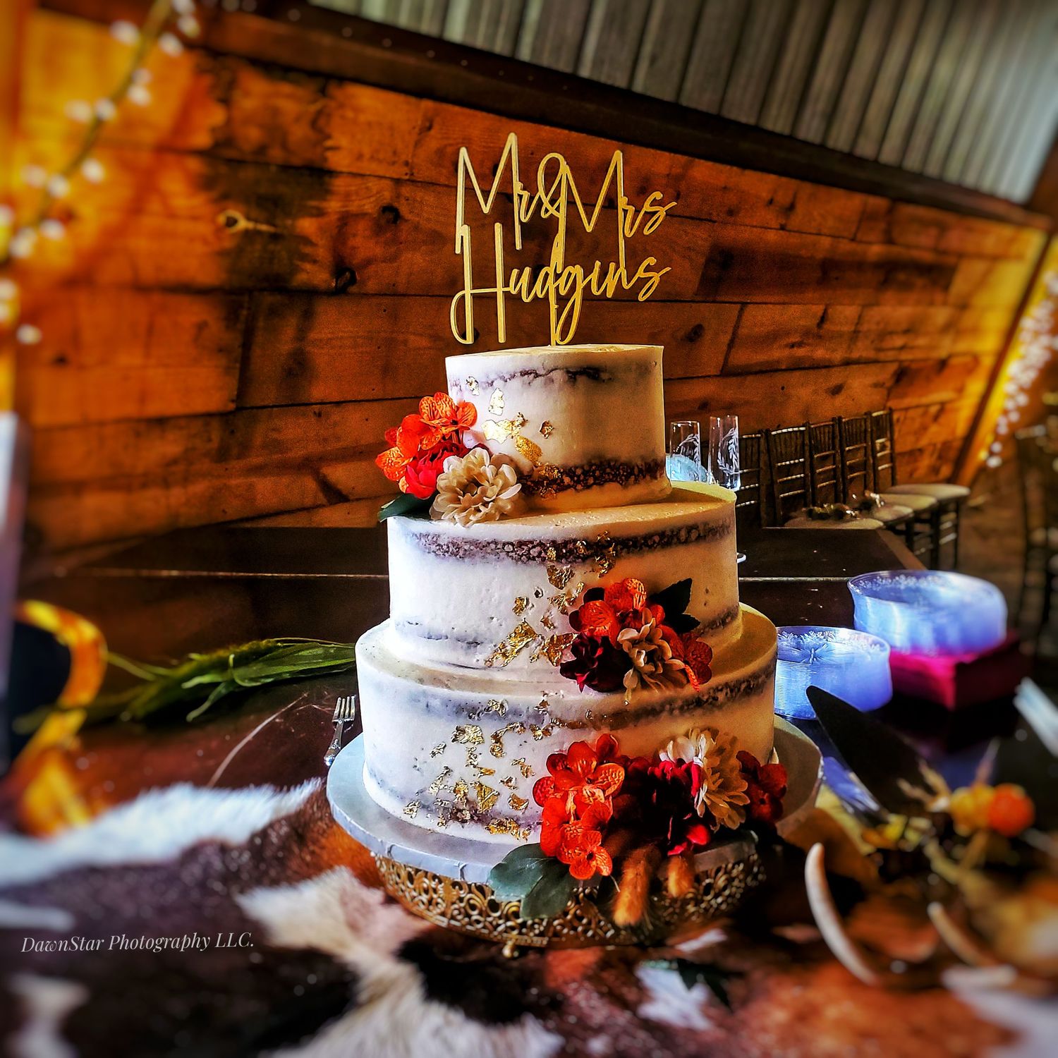 A rustic wedding cake with textured frosting and coral flowers sits on a wooden table in warm lighting.