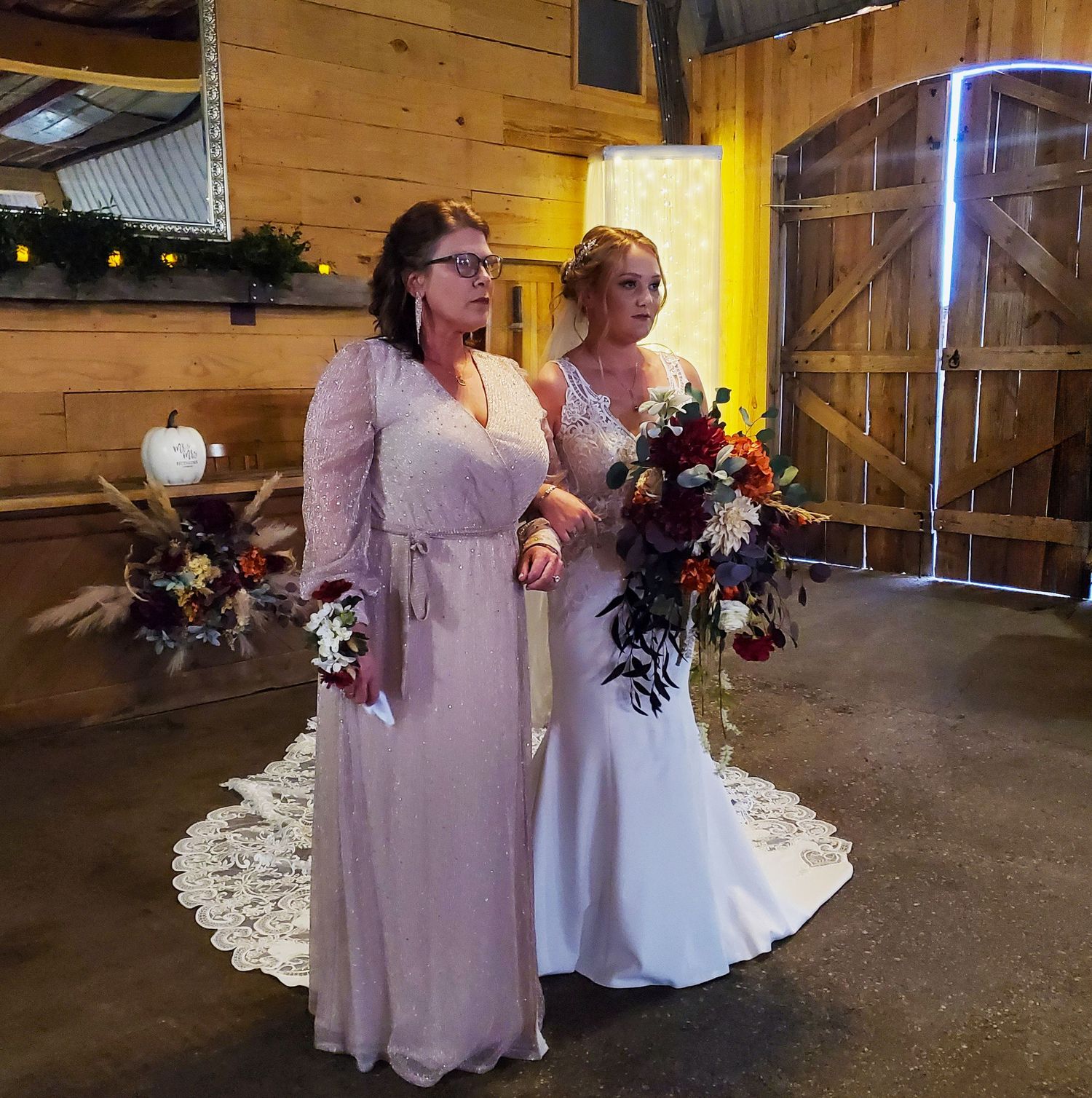 Two people in formal attire stand together on a rustic wooden floor surrounded by flower petals at a wedding venue.