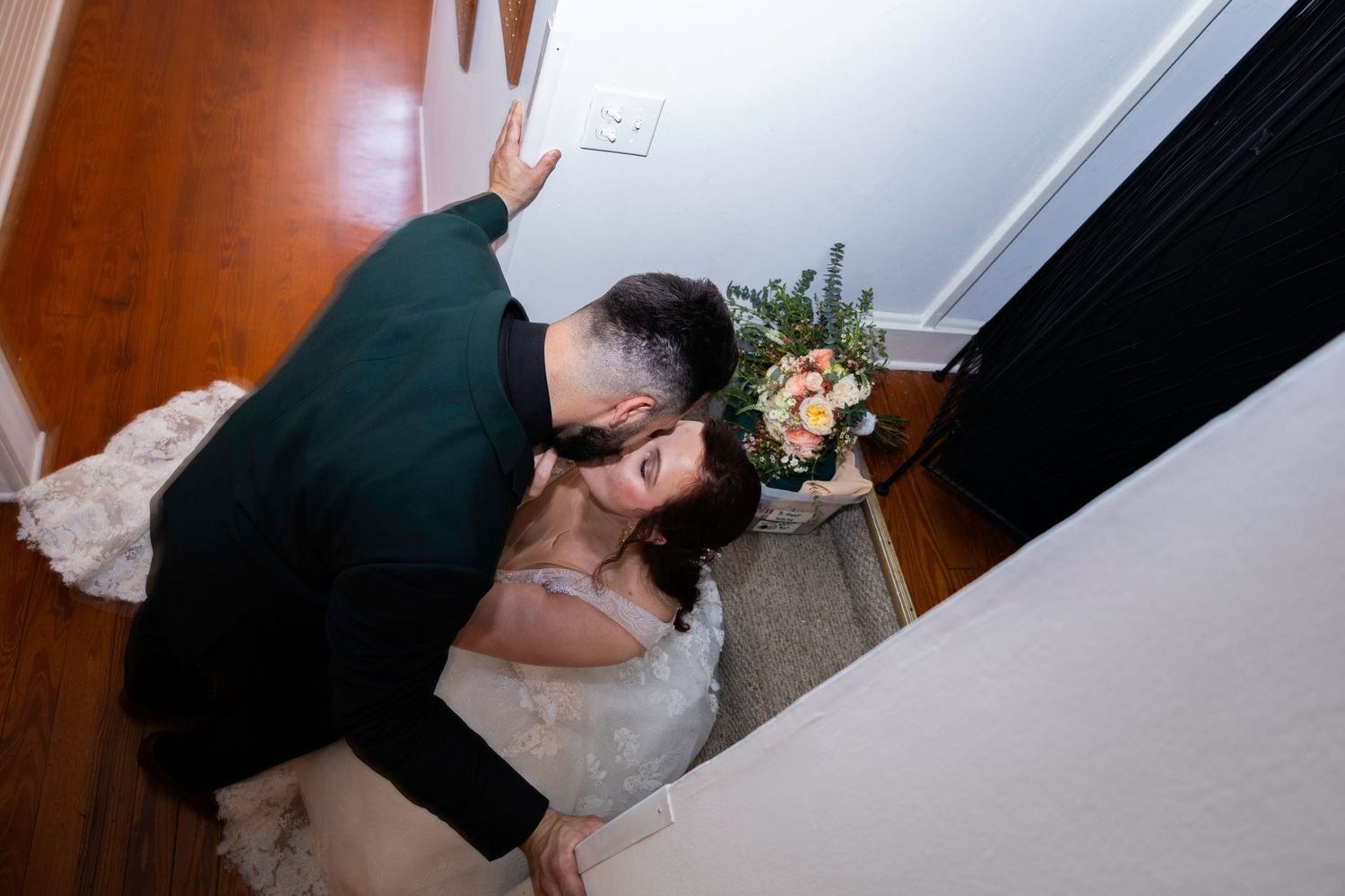 Bride and groom sharing a romantic kiss on staircase, bride holding a colorful bouquet, wedding day moment.