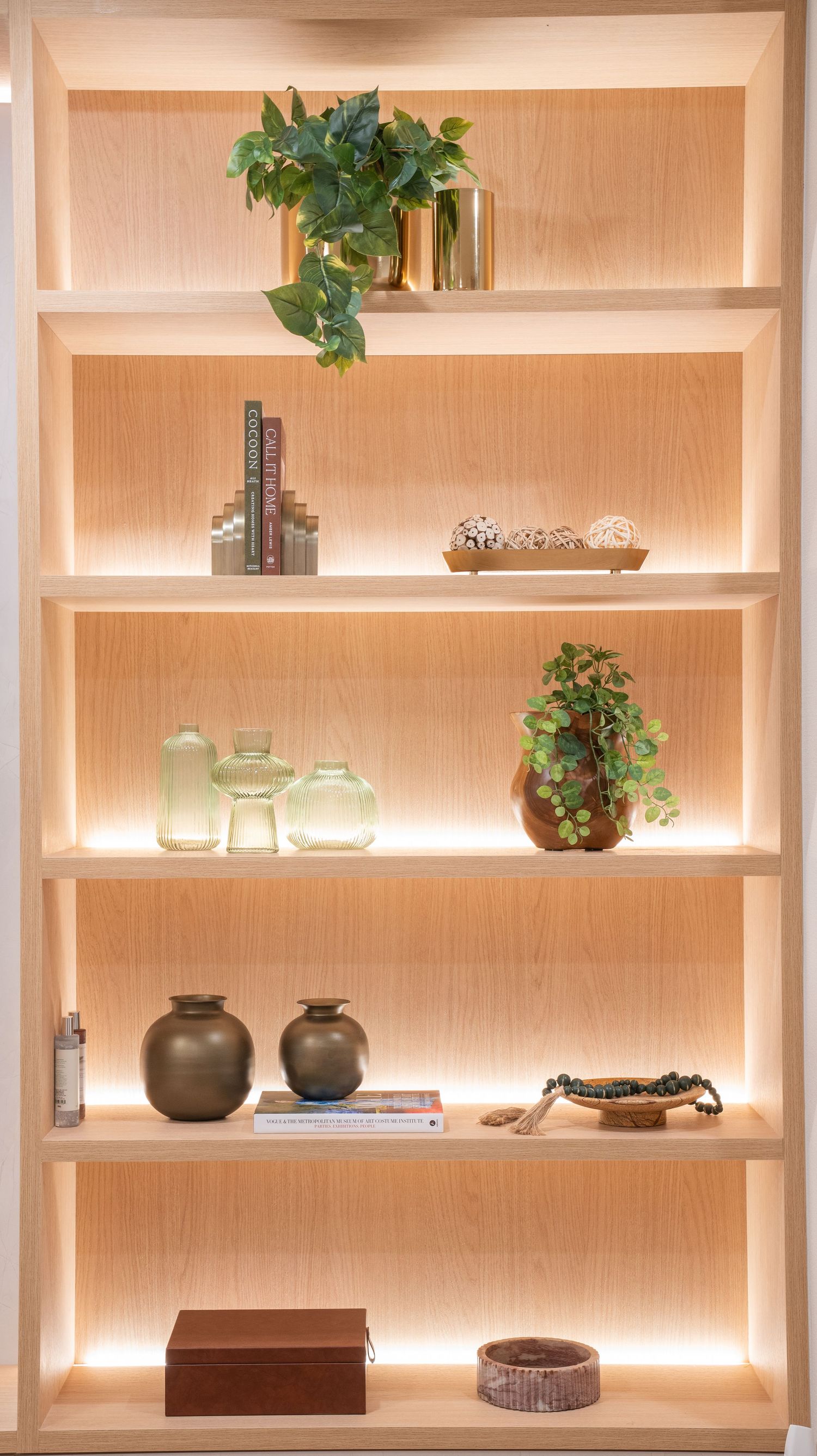 Modern wooden shelving unit with LED backlighting displays decorative items including plants, vases, books and ornamental objects.