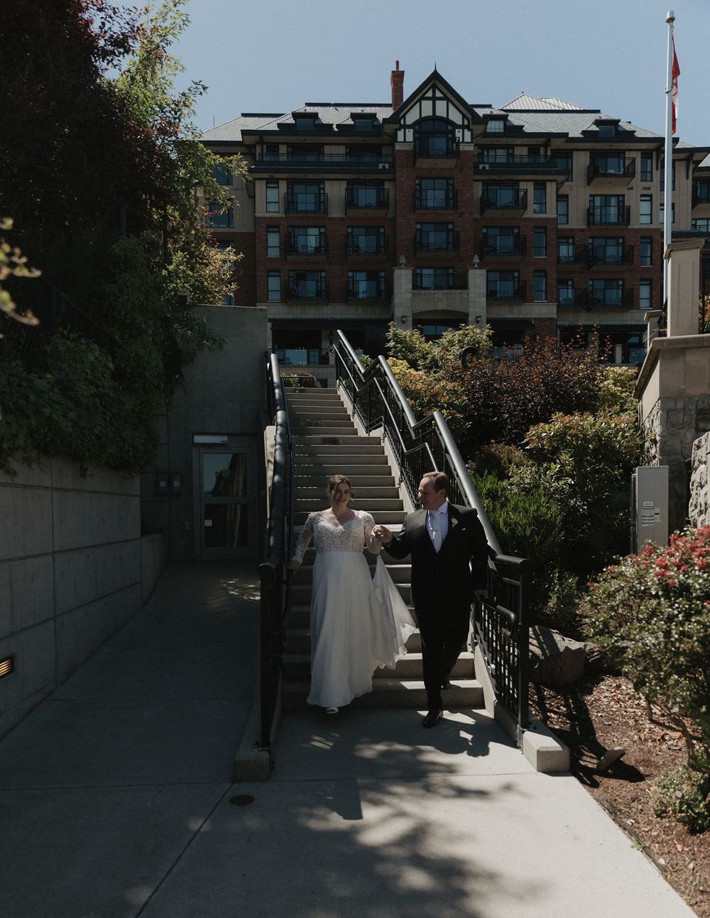 Bride and groom walk hand in hand down outdoor stairs with a grand Tudor-style hotel building behind them.