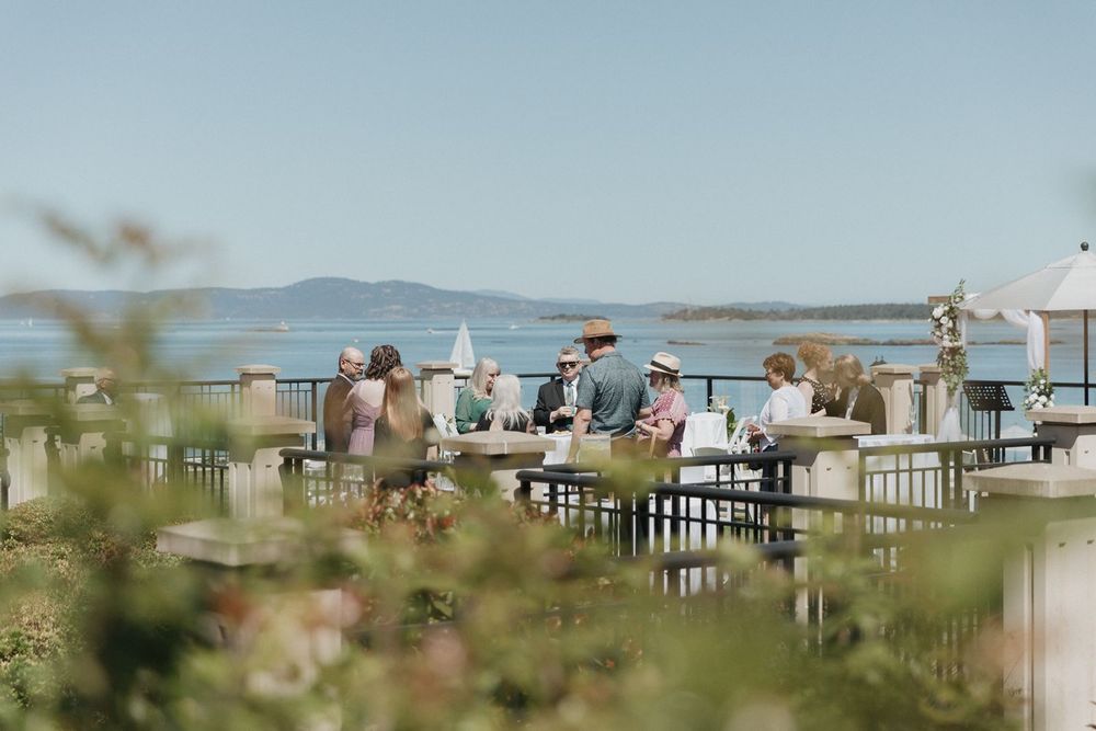 Guests dining outdoors at a waterfront wedding reception with scenic ocean and mountain views.