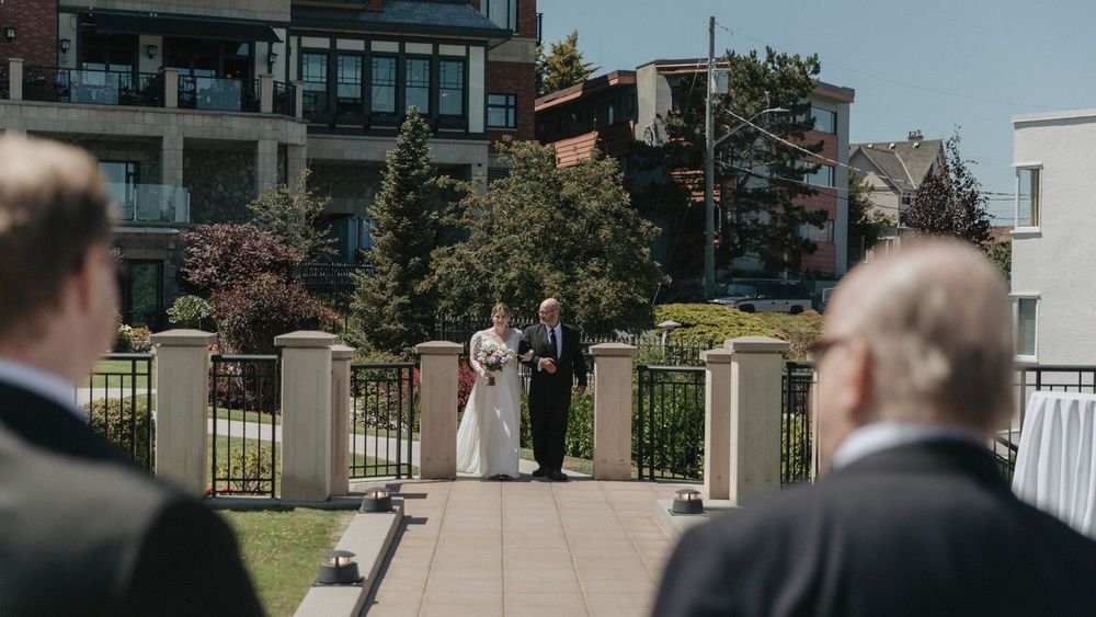 Bride walks down the aisle with escort at an outdoor waterfront wedding ceremony.