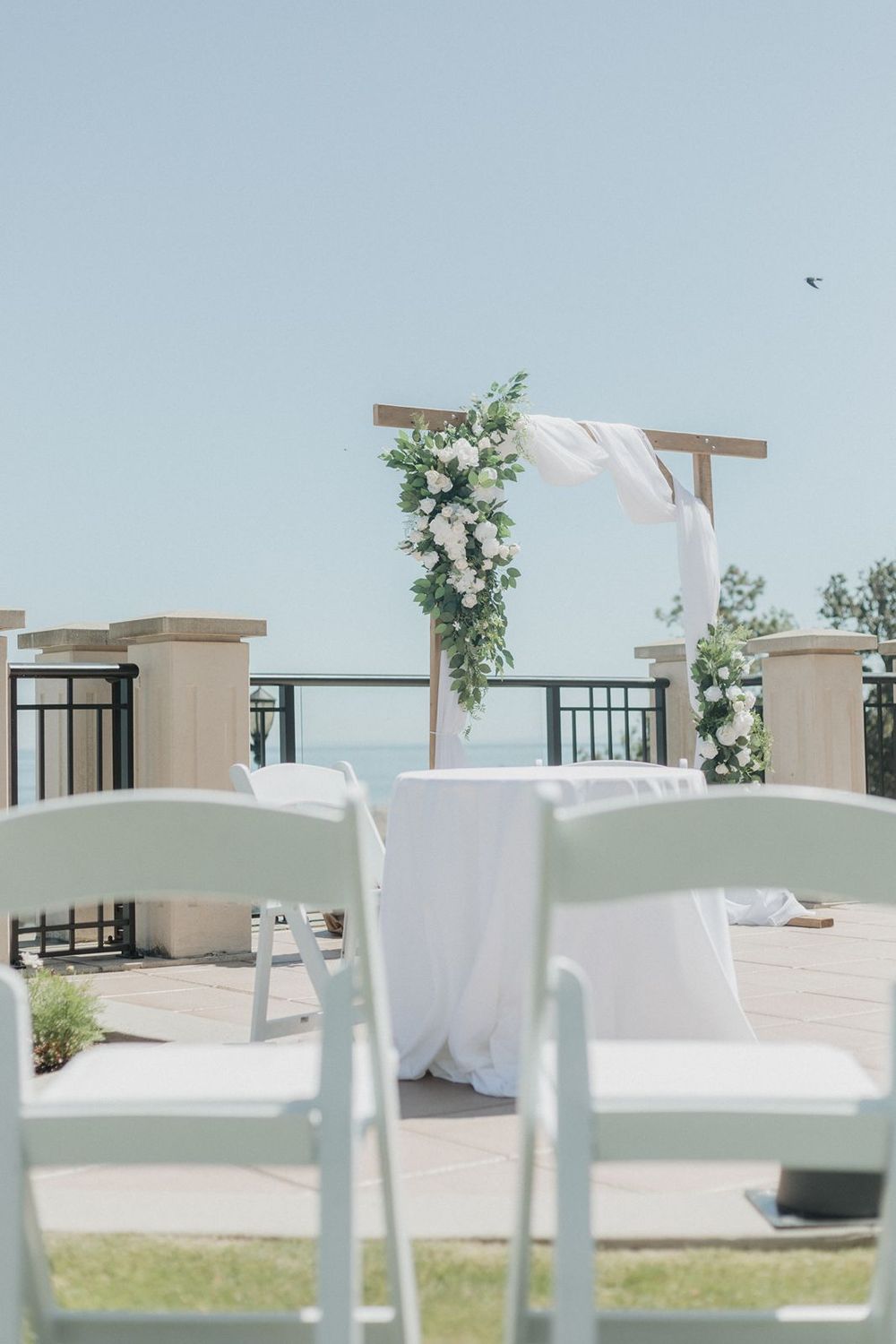Elegant wooden wedding arch with white floral and greenery decor overlooking a serene waterfront.