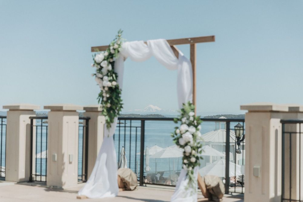 Beautiful wooden wedding arch adorned with white flowers, greenery, and draped fabric by the sea.