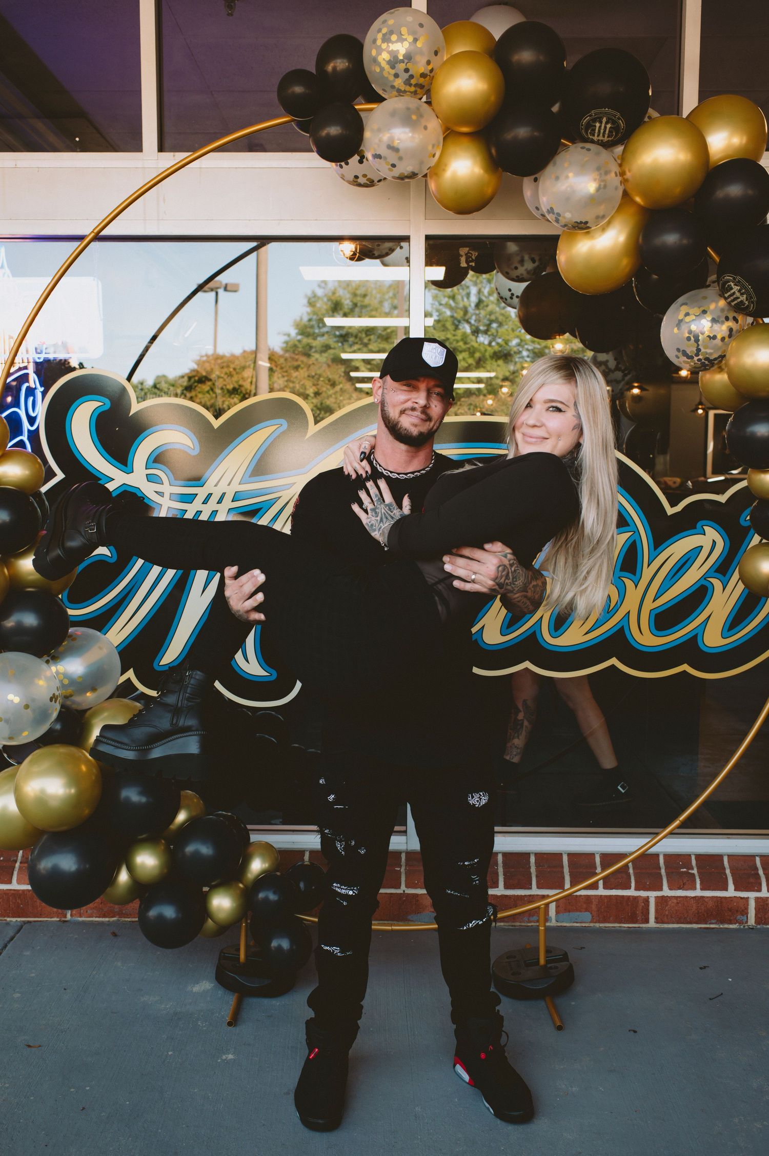 A festive party setup with black and gold balloons decorating a wall with neon signage.