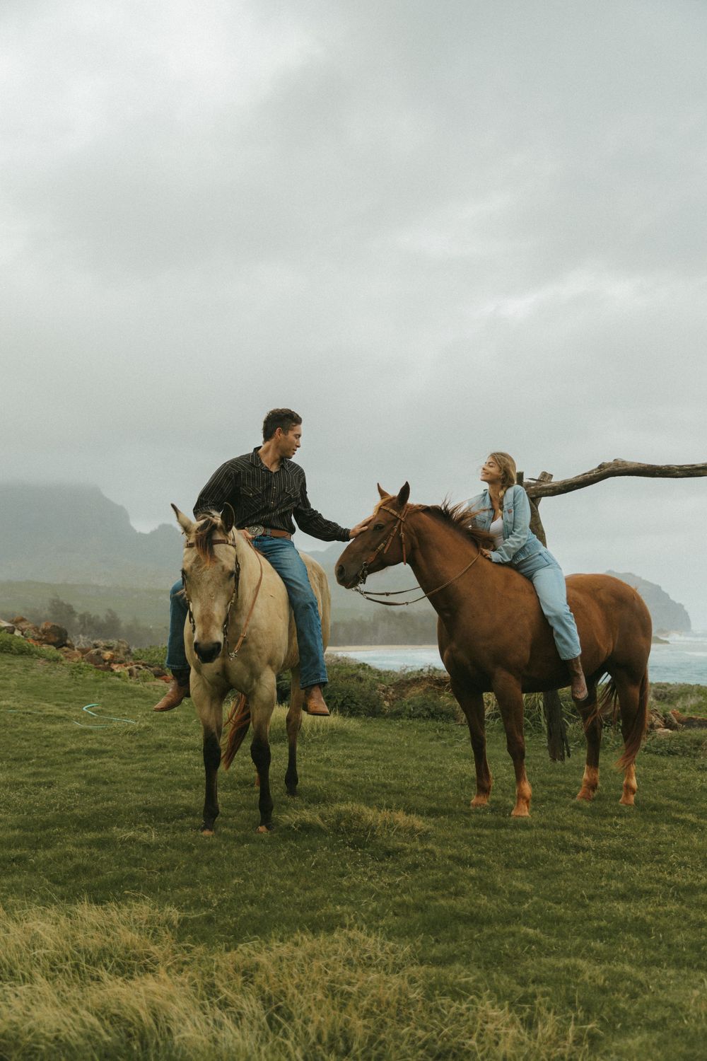 Riders on horseback exploring a scenic coastal trail with mountains in the background.