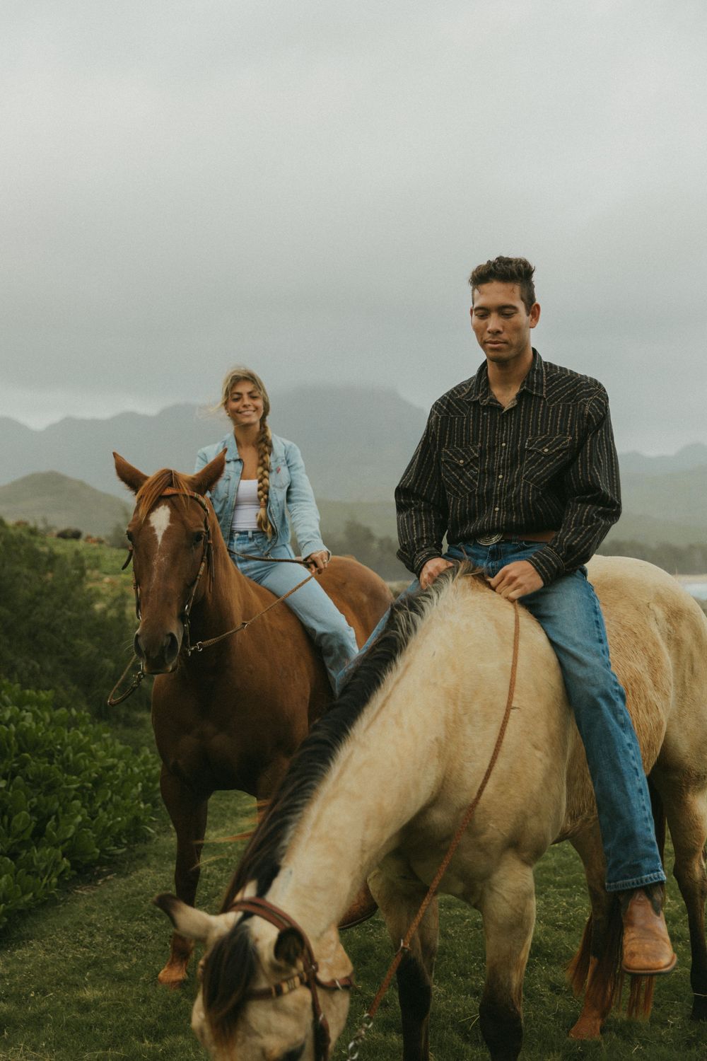Riders mounted on brown and cream colored horses against a misty coastal landscape.
