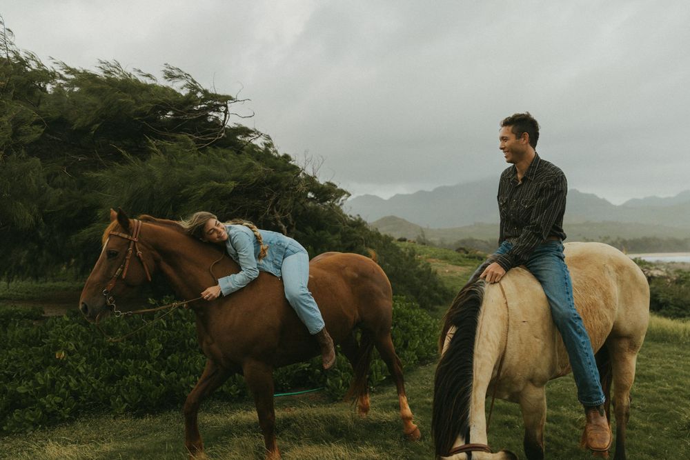 Riders on horseback traversing a green hillside with ocean views in the distance.