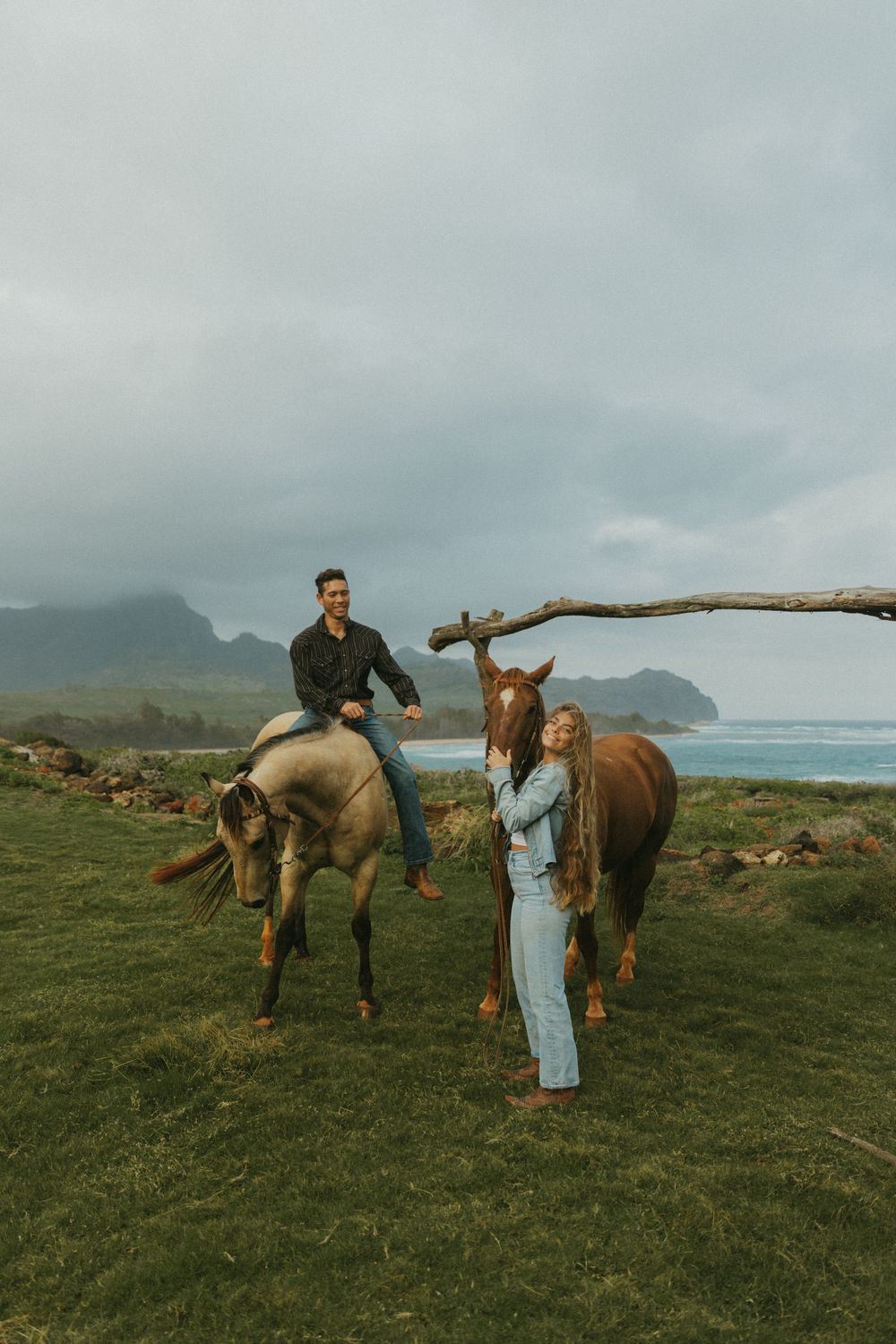 Group gathered with horses on a grassy cliff overlooking the ocean and mountains.