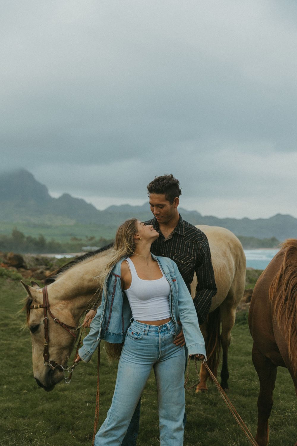 Couple with horses on scenic coastal grassland with mountains and ocean views.