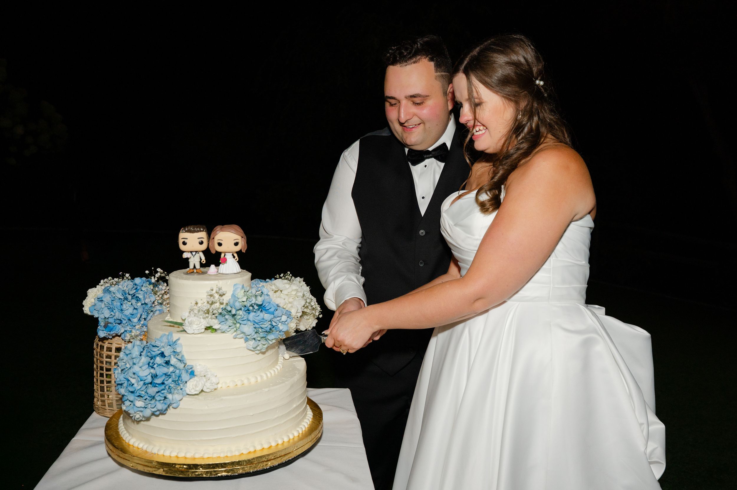A bride and groom cut their wedding cake with custom bobbleheads at their reception in Brewster, NY in Hudson Valley.