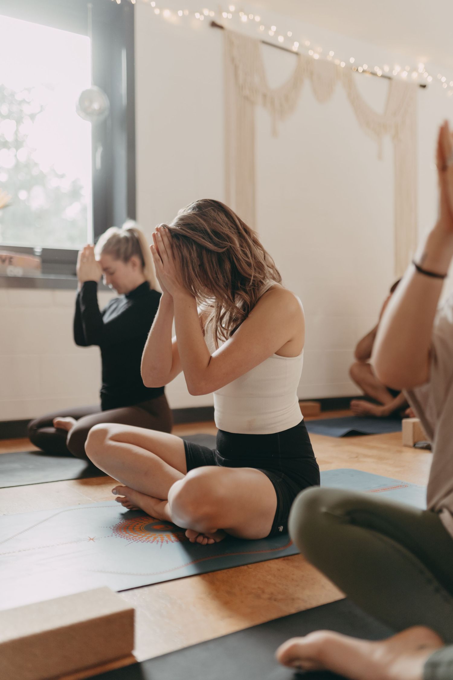 A group of people practicing yoga and stretching exercises on mats in a dimly lit studio with string lights.