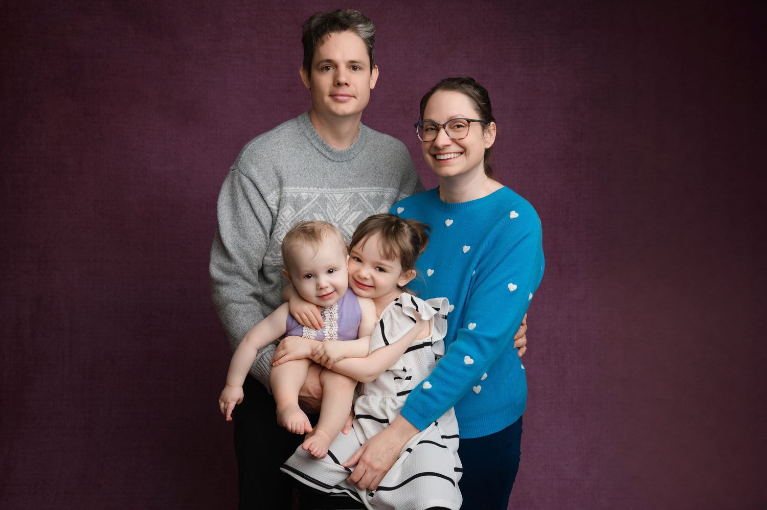 Studio portrait of a family of four against a dark burgundy background.