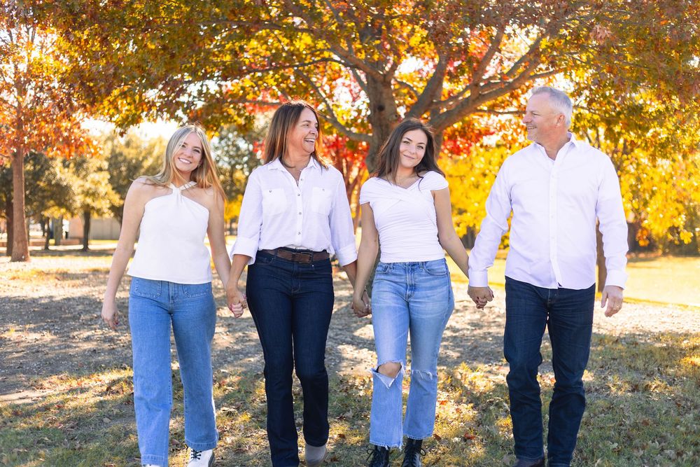 A group of four people walking together on a path with autumn trees and golden sunlight in the background.