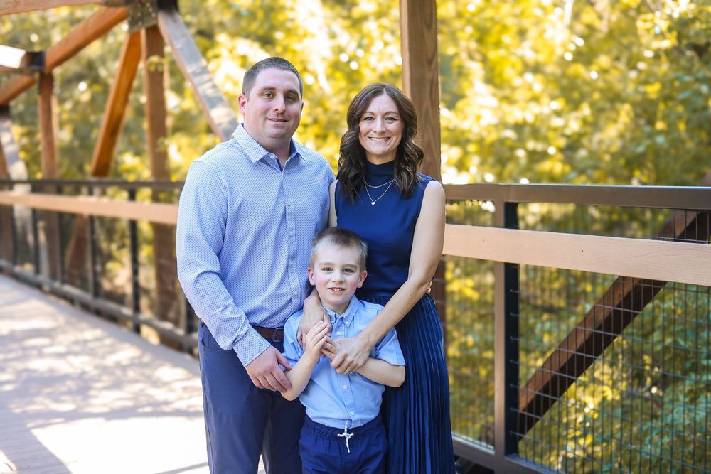 Family in coordinating blue outfits poses together on wooden bridge during autumn outdoor photo session.