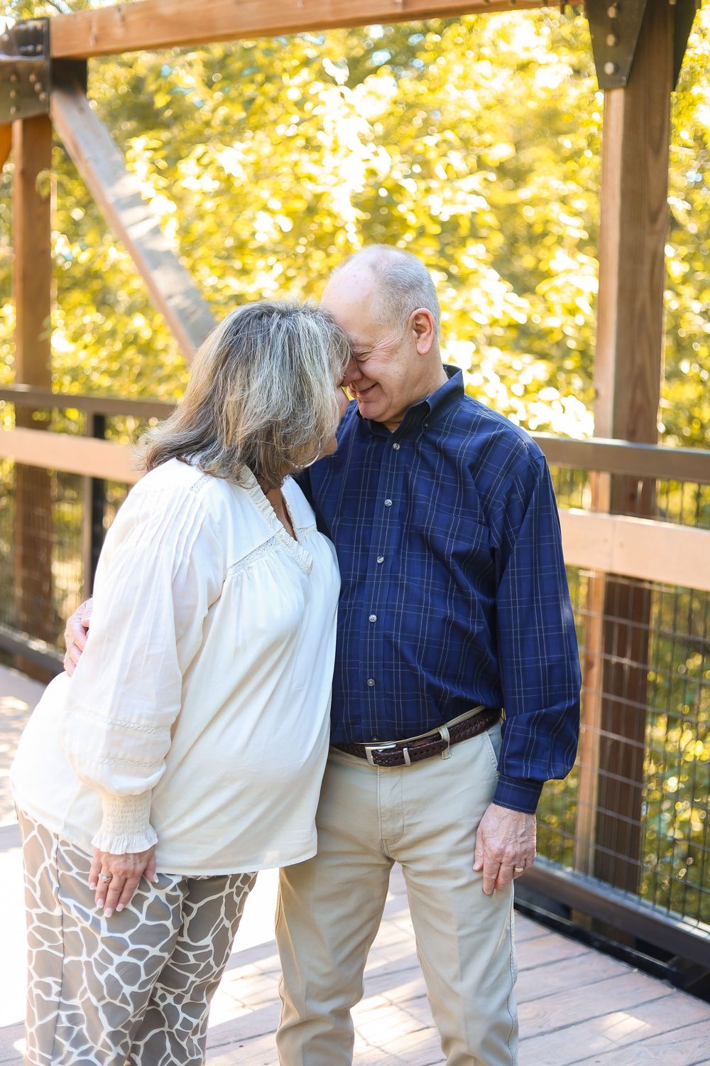 Senior couple sharing an intimate moment on a wooden deck surrounded by golden autumn foliage.