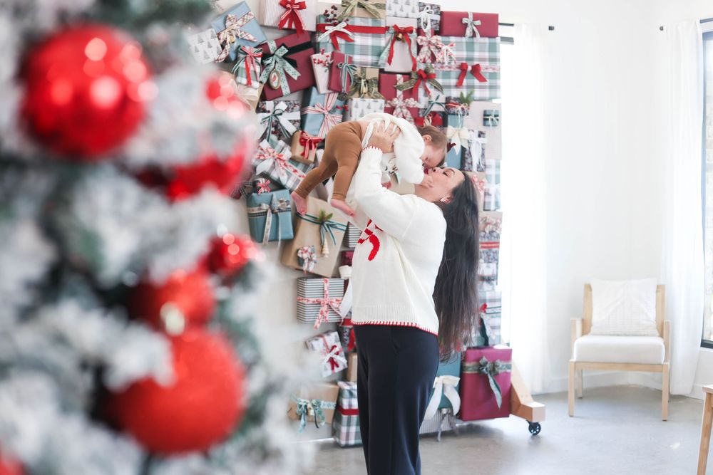 A white Christmas tree decorated with red ornaments and gift boxes stands in a bright modern room.