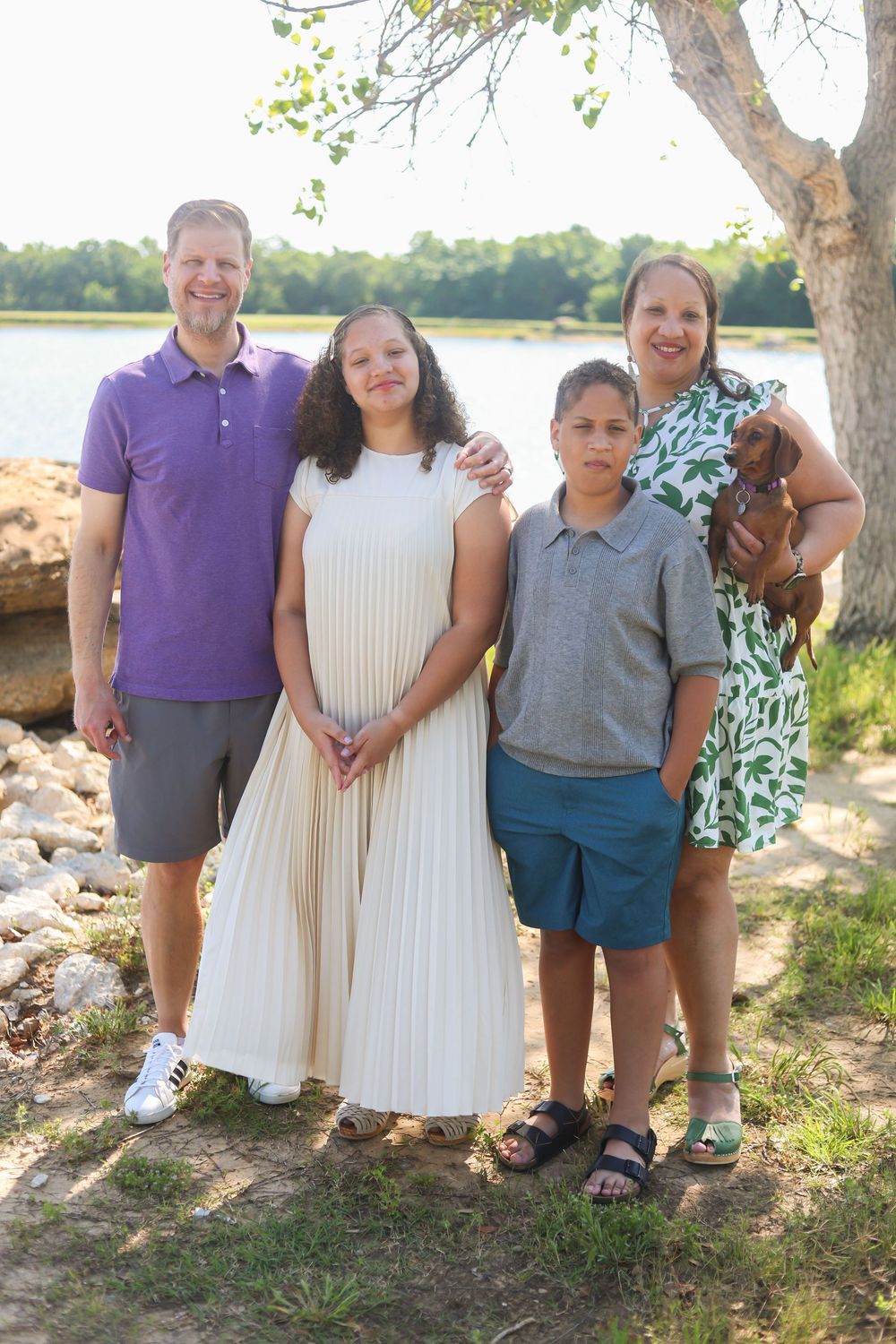 A family poses together outdoors in coordinated purple and white outfits near a scenic waterfront setting.