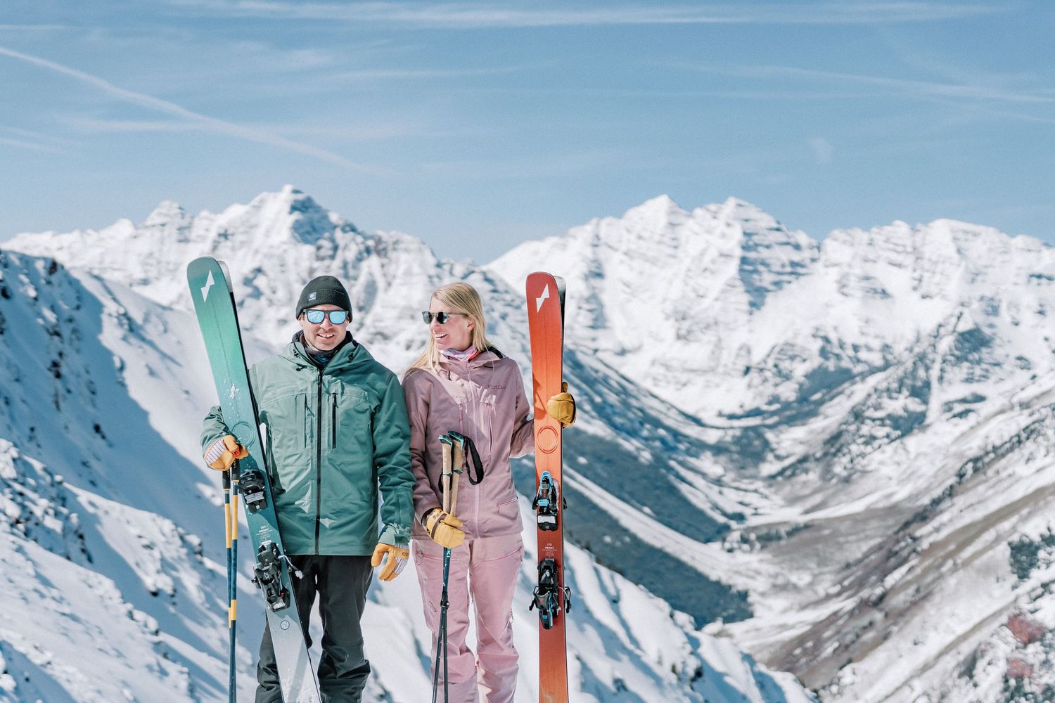 Two figures stand at a scenic mountain overlook in Rocky Mountain National Park with dramatic peaks in the distance.