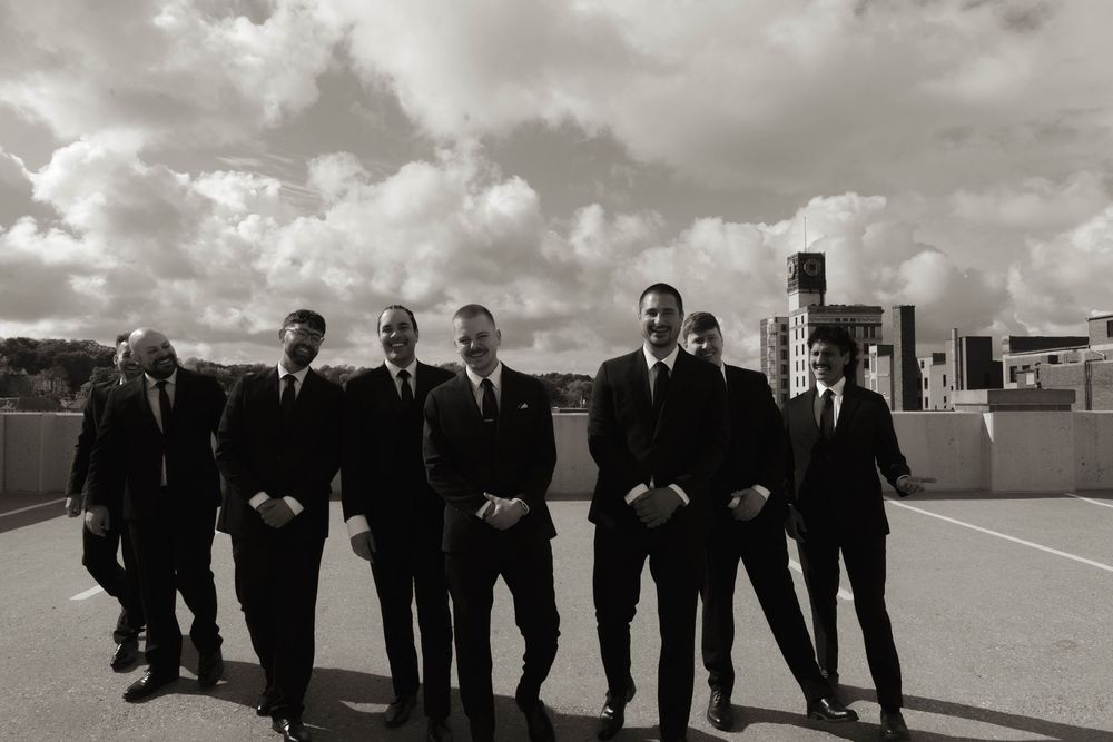 Groomsmen in dark suits pose casually on a rooftop with urban architecture in the background.
