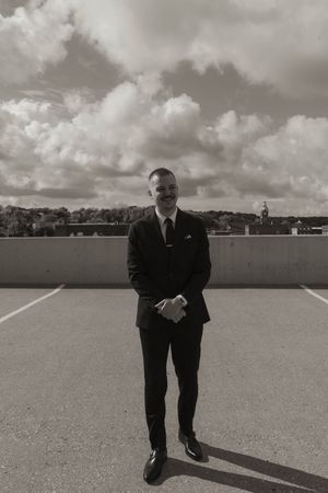A suited figure stands alone on a rooftop parking area under cloudy skies.