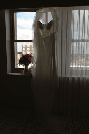White wedding dress hanging in front of sunlit window creating a silhouette effect.