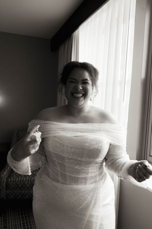 Person in off-shoulder wedding dress expressing joy near window.
