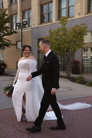 Couple in wedding attire sharing playful moment outside brick building.
