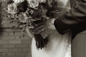 Close-up of a wedding bouquet with roses being held against a white dress.