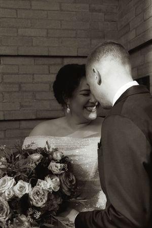 An intimate moment between newlyweds sharing laughter against a brick wall.