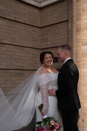 A romantic wedding moment captured against brick walls with flowing veil and vibrant bouquet.