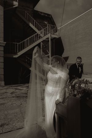 A wedding couple posing near an outdoor staircase with flowing veil.
