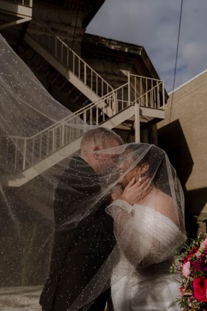 A romantic moment captured through a flowing veil near an outdoor staircase.