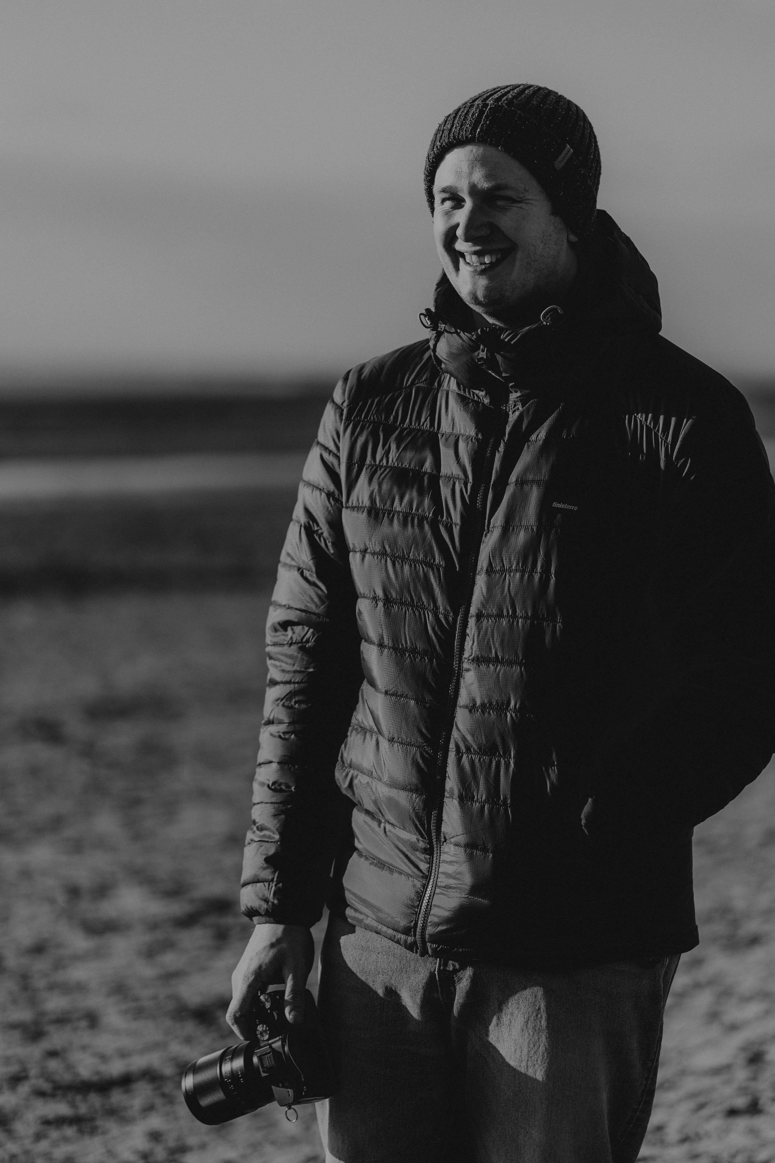 Person wearing a bright orange puffer jacket and grey beanie smiles while standing outdoors in winter weather.