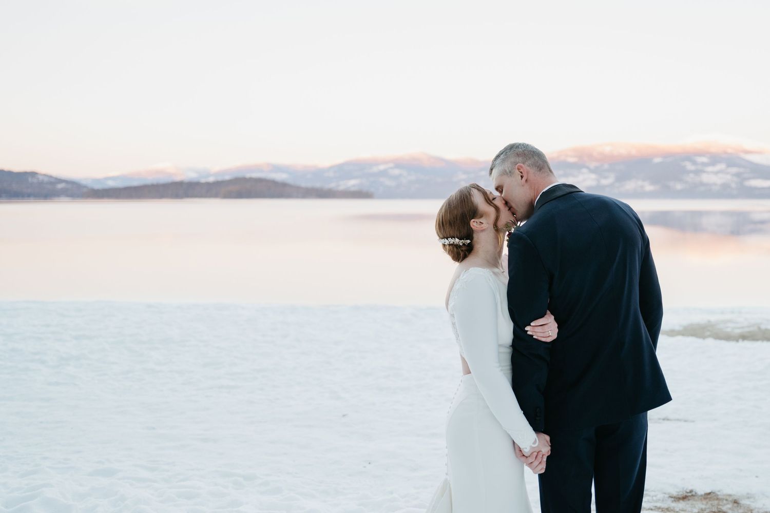 A couple shares a romantic moment at sunset on a beach with mountains in the background.