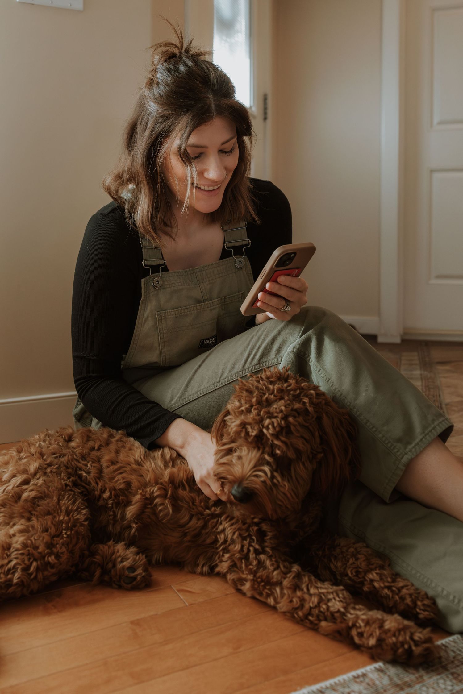 A person in olive green lounges on the floor while petting a fluffy brown goldendoodle dog.