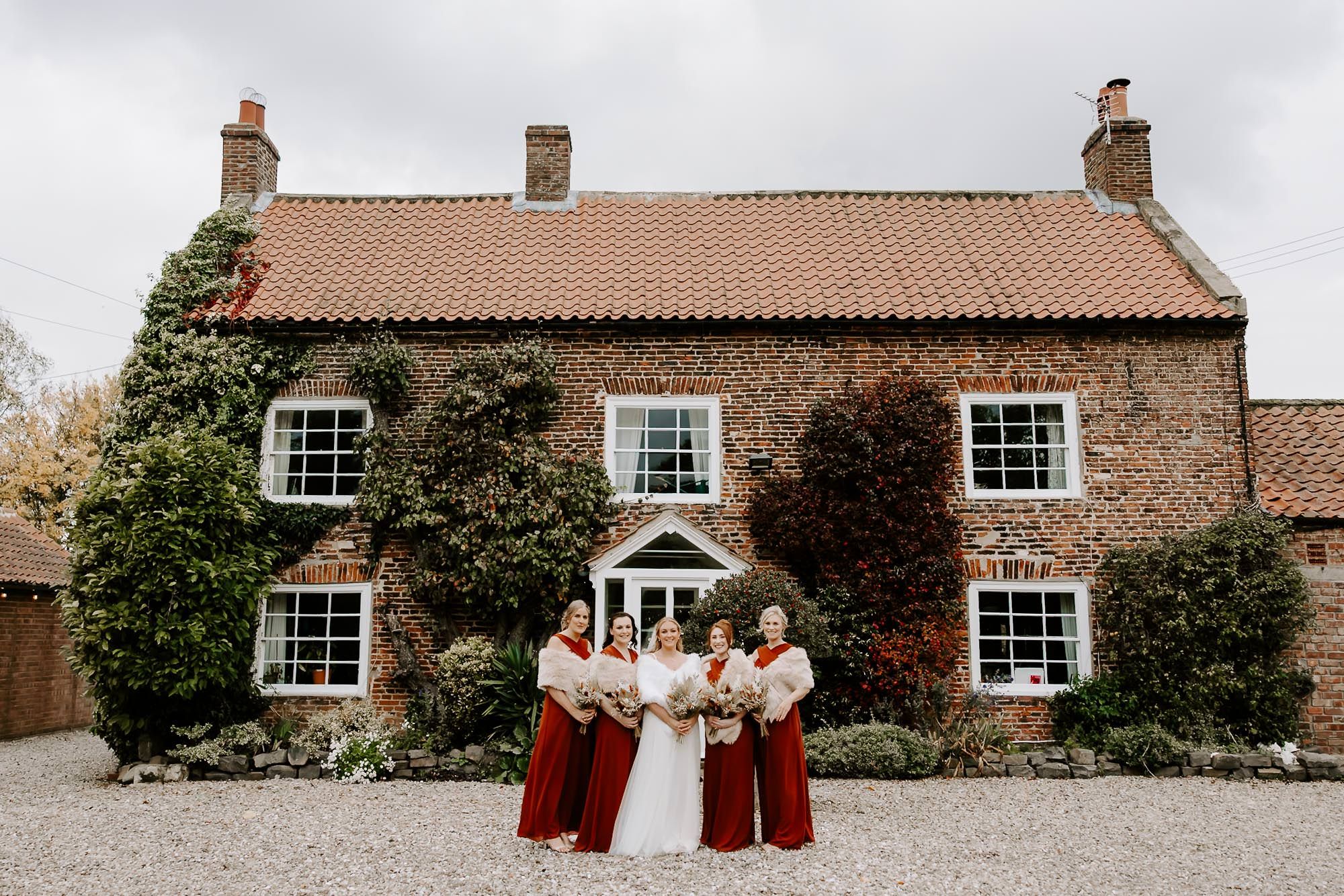 A series of wedding party photos taken outside a rustic brick farmhouse with white trim windows.