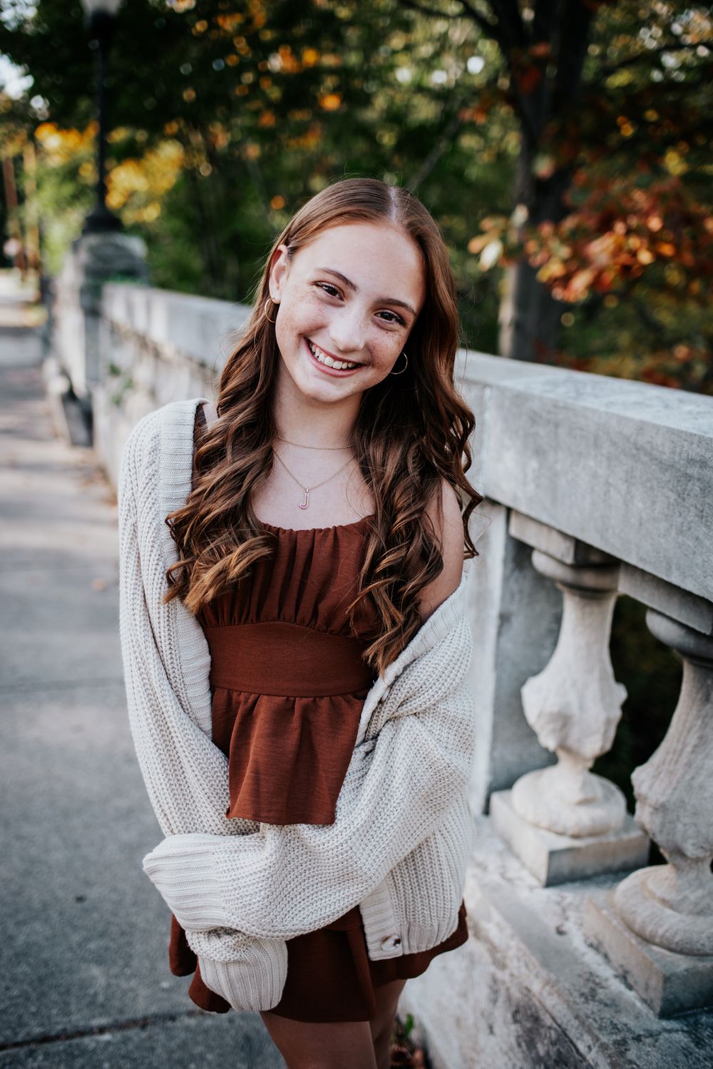 Portrait on stone bridge with autumn foliage in background.